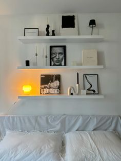 a bed with white sheets and pillows in a room that has shelves on the wall above it