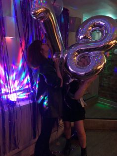 two women holding up large balloons in front of a wall with lights on it and the number 8