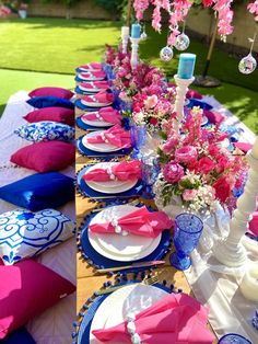 the table is set with pink and blue plates, napkins, and vases