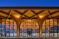 an architecturally designed building with large windows and wooden beams on the outside, lit up at night