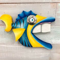 a blue and yellow fish with an eye on it's face is mounted to the side of a wooden wall