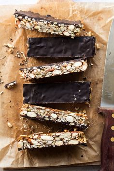 five pieces of chocolate and nuts on top of a piece of parchment paper next to a knife