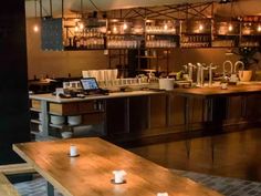 an empty restaurant with wooden tables and candles on the counter, in front of shelves filled with wine glasses