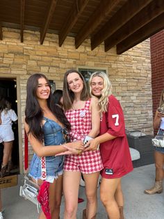 three young women standing next to each other in front of a brick wall and door