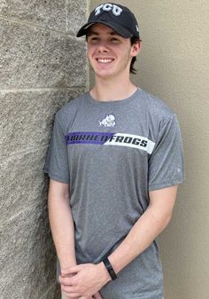 a young man standing next to a stone wall wearing a hat and smiling at the camera