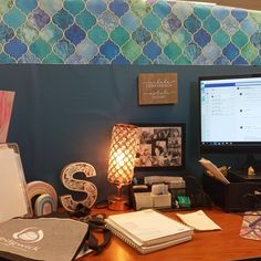 a desk with a computer monitor, lamp and other items on it in front of a blue wall