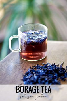 a glass cup filled with blue tea next to a pile of dried lavender on top of a wooden table