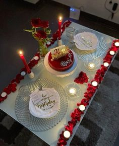 a table topped with two cakes covered in frosting and red roses next to candles