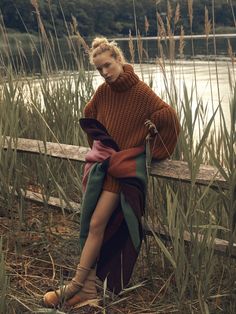 a woman is sitting on a bench by the water wearing a sweater and high heels