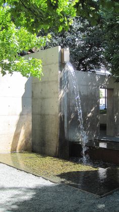 a water fountain in the middle of a park with trees surrounding it and sunlight shining on the ground