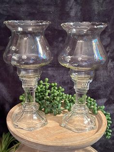 two clear glass vases sitting on top of a wooden stand