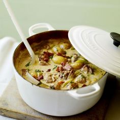 a white pot filled with food sitting on top of a wooden cutting board next to a spoon