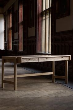 a wooden bench sitting in front of a window next to a wall with large windows