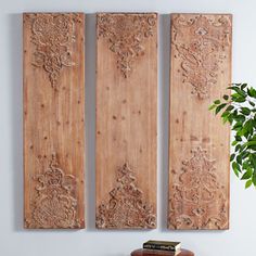 three wooden panels are hanging on the wall next to a potted plant and books