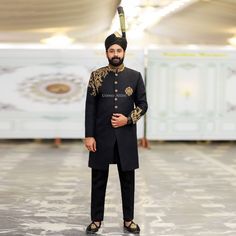 Luxurious Black Fabric: The sherwani is made of a high-quality black fabric, providing a sophisticated and formal look. Elaborate Golden Embroidery: The sherwani is adorned with intricate golden floral embroidery and embellishments across the front and sleeves. This adds a rich, ornate touch to the garment. High Collar: The sherwani has a high, upturned collar that accentuates the formal, regal appearance. Decorative Buttons: The center of the sherwani features a row of embroidered buttons that Black Sherwani With Gold Embroidery For Festive Occasions, Traditional Black Embroidered Sherwani, Elegant Embroidered Black Sherwani, Traditional Black Embellished Sherwani, Black Embroidered Semi-stitched Sherwani, Black Tuxedo Suit, Waistcoat Designs, Prince Coat, Sherwani Groom