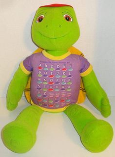 a green stuffed turtle with a purple t - shirt on it's chest and alphabets on its back