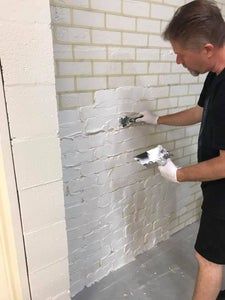 a man in black shirt and white gloves painting a brick wall with paint rollers