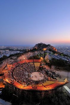 an aerial view of a concert on top of a hill at night with the city in the background