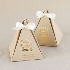 two small paper pyramids with white bows on the top one has gold foil lettering