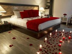 a bed with rose petals on the floor next to lamps and candles in front of it