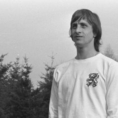 black and white photograph of a man with long hair holding a frisbee in front of trees