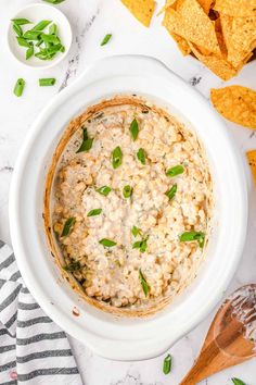 a white bowl filled with dip surrounded by tortilla chips and cilantro