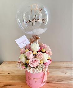 a bouquet of flowers in a pink box with a balloon