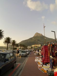 cars parked on the side of a road next to a hill with a mountain in the background