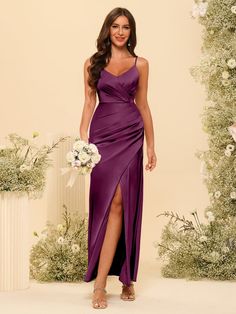 a woman in a long purple dress standing next to a flower arrangement and holding a bouquet