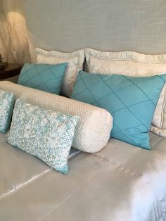 a bed with blue and white pillows on it's headboard, next to a night stand