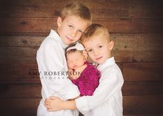 three children hugging each other in front of a wooden wall