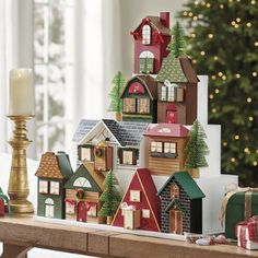 a wooden table topped with lots of small christmas village houses next to a lit candle