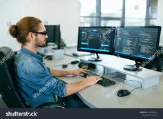 a man sitting at a desk with two computer monitors and keyboard in front of him