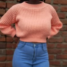 a woman wearing high waist jeans and a pink sweater stands in front of a brick wall