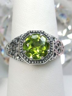 Natural Peridot RingNew Vic Design#D11 Inspired by Victorian and Edwardian designs, this stunning antique reproduction ring is crafted in white gold. This gorgeous ring is set with a flawless round natural peridot. The stunning gemstone is 8mm in diameter. The band is marked 925 (sterling silver),10k or 14k as chosen. Notice the beautifully intricate design of the silver filigree setting and band. The delicate swirl filigree craftsmanship travels down the band and morphs into angular accents. Th Classic Peridot Birthstone Jewelry, Classic Peridot Jewelry For May Birthstone, Classic Peridot Jewelry With Prong Setting, Classic Peridot Jewelry With Accent Stones, Vintage Green Rings With Accent Stones, Antique Green Rings With Prong Setting, Classic Peridot Ring Jewelry, Vintage Green Filigree Ring With Gemstone, Classic Peridot Green Rings