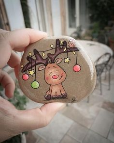 a hand holding a rock with a drawing of a reindeer and christmas lights on it