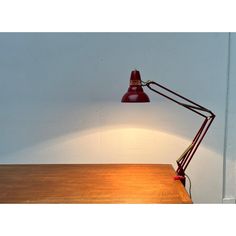 a red desk lamp sitting on top of a wooden table next to a white wall