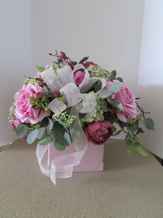 a bouquet of pink roses and greenery sits in a box on a table top