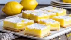 lemon bars on a white plate with some lemons in the backgroung