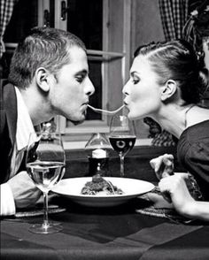 a man and woman sitting at a table with wine glasses in front of their mouths