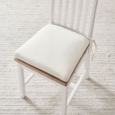 a white wooden chair with a cushion on the back and seat pad, in front of a carpeted floor