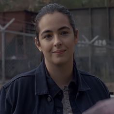 a young woman is smiling and looking at the camera while standing in front of a chain link fence