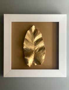 a gold leaf mounted in a white frame