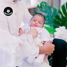 a man holding a baby in his lap while another person holds him up to their chest