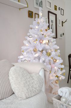 a white christmas tree in a living room next to a couch and table with pictures on the wall