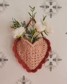 a crocheted heart hanging on the wall with white flowers in front of it