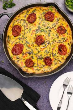 a pizza sitting on top of a pan covered in cheese and toppings next to silverware