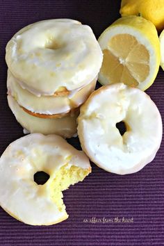 lemon donuts with white frosting and sliced lemons on a purple mat next to them