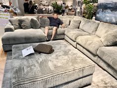 a man sitting on top of a gray couch in a living room filled with furniture