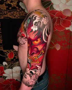 a man with a colorful tattoo on his arm and shoulder is standing in front of a red wall